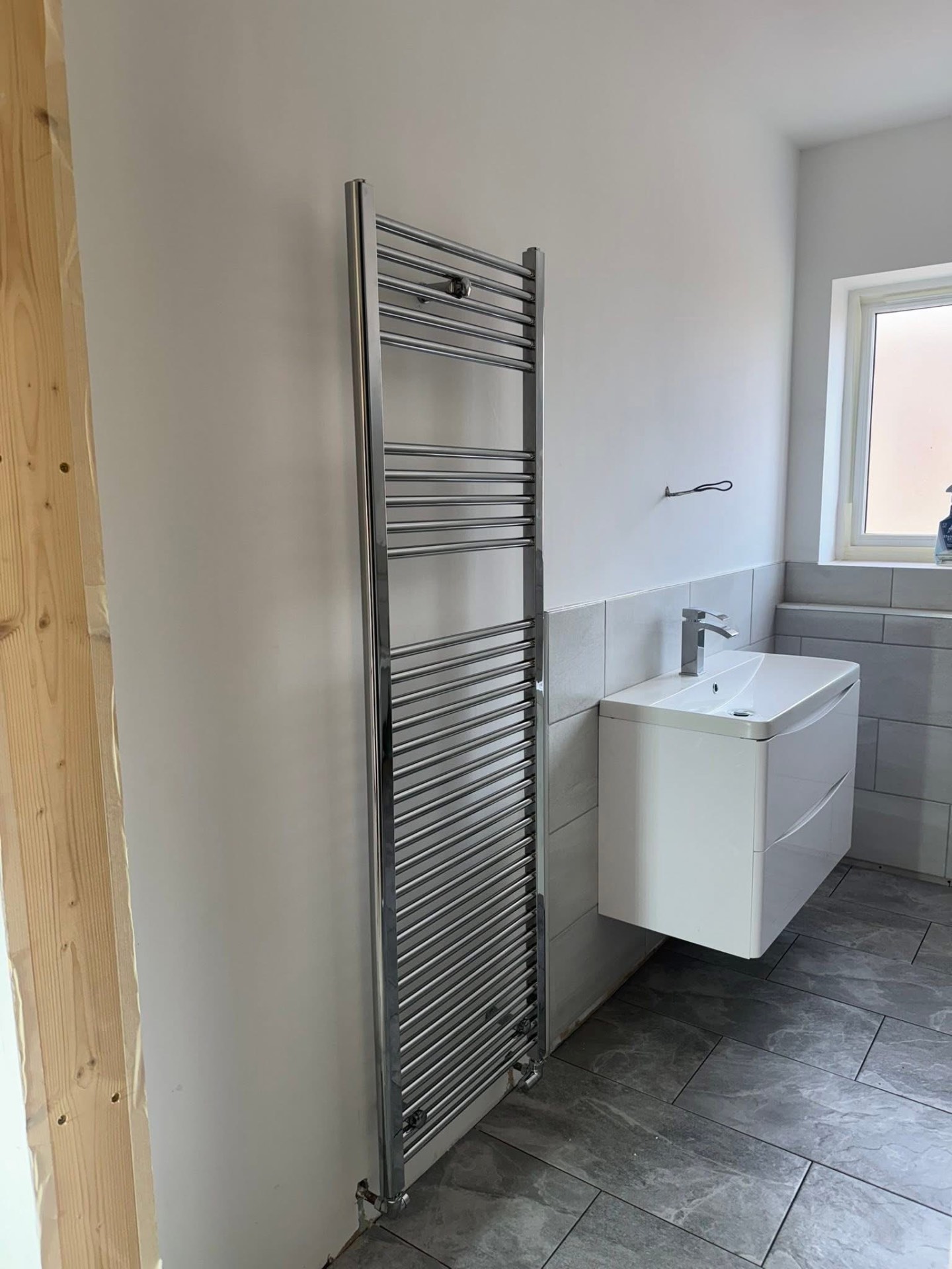 Modern bathroom with chrome towel radiator and floating vanity unit installed by Leighton Plumbing and Heating