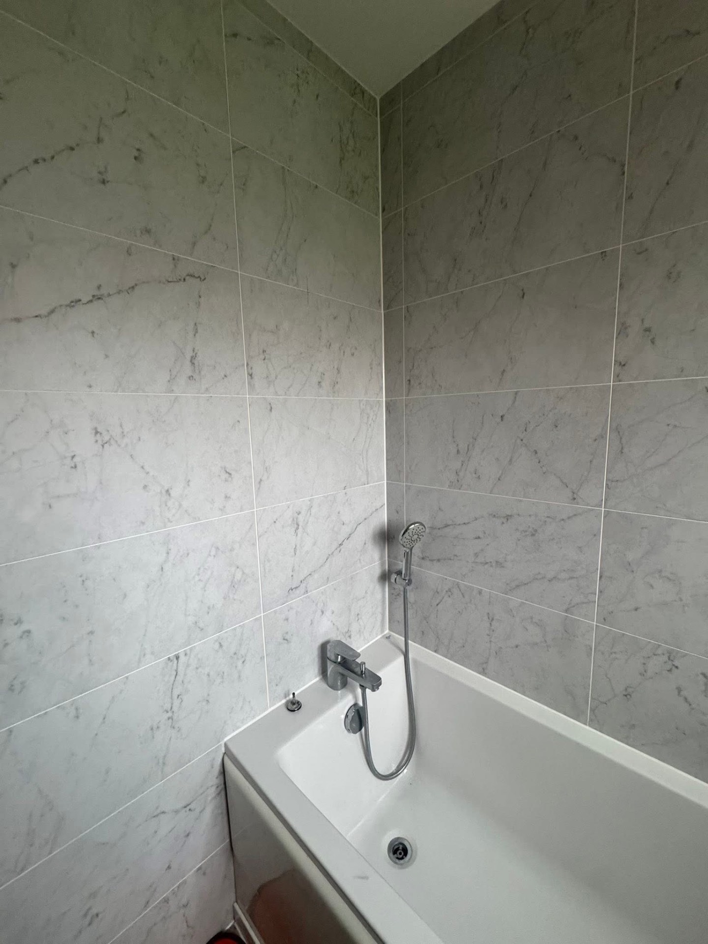 White acrylic bathtub with chrome mixer tap and marble-effect surround